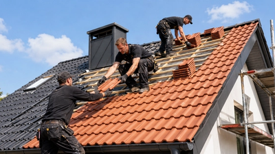 Drei Dachdecker decken ein Dach mit roten Ziegeln.